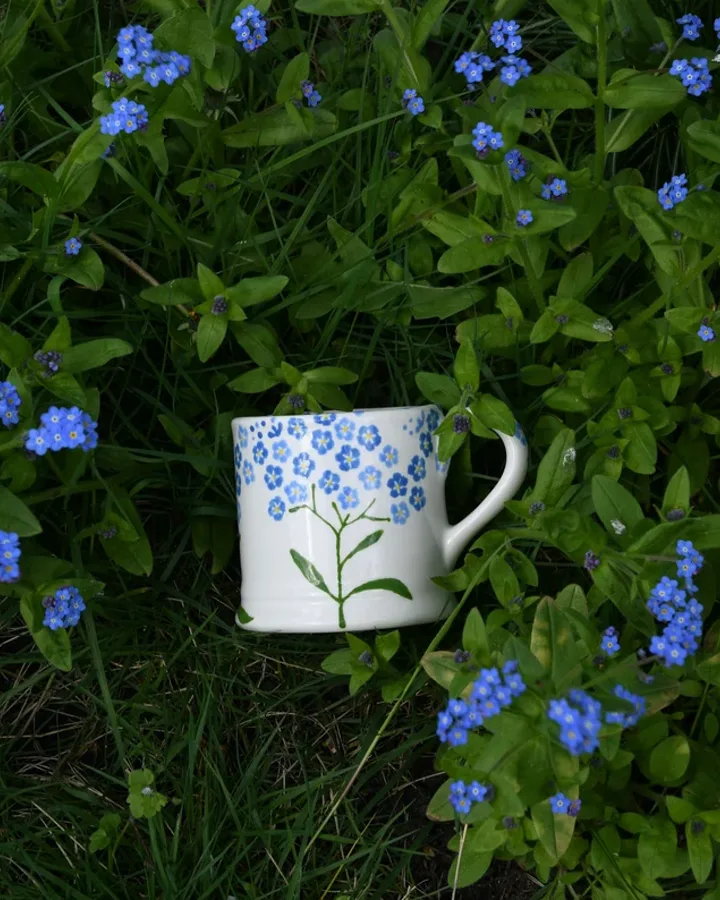 Hand-painted forget-me-not mug among wild flowers